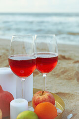 Tray with glasses of wine, fruits and candles on sandy sea beach