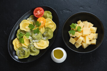 Ravioli served with grated parmesan cheese, flatlay on a black stone background, horizontal shot