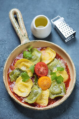 Beige serving pan with ravioli on tomato sauce bedding, vertical shot on a blue stone background