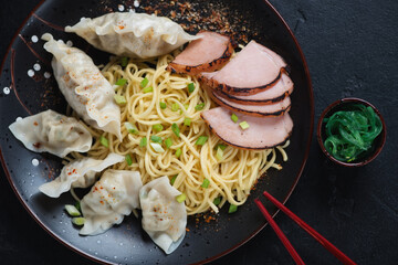 Kon Loh Wantan Mee or egg noodles with wontons and chinese bbq pork served on a black plate, above...
