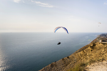 A paraglider flies over mountains and sea in a blue sky on a Sunny summer day.