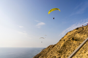 A paraglider flies over mountains and sea in a blue sky on a Sunny summer day.