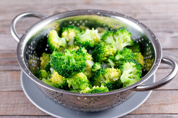 Blanched broccoli in colander on a wooden background. Healthy diet. Colander with fresh green broccoli on table