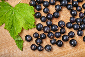 Fresh ripe black currants heap on wooden background. Natural organic berries with green leaves scattered on weathered wooden table, new berry harvest. Top view
