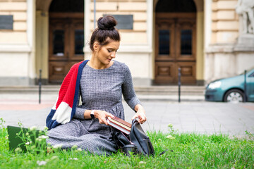 Obraz premium Young adult female student puts books to backpack sitting on grass near university building
