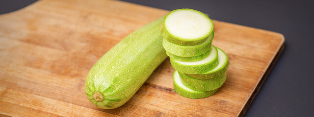 Slices of courgettes on wooden chopping board. Fresh green zucchini whole and cut into slices on cutting board