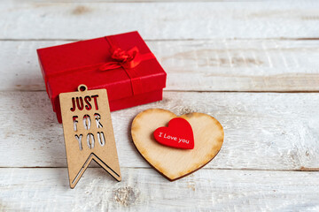 Red gift box and two hearts on a white wooden background. Texts I love you and just for you.