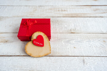 Red gift box and two hearts on a white wooden background. Text I love you.