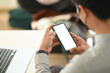 Cropped shot of businessman hands using smartphone mockup at the white office desk. Blank screen mobile phone for graphic display montage.