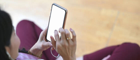 Cropped shot of young woman sitting at home on couch and using smartphone with blank screen surfing internet.