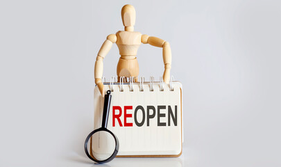 Wooden man shows with a hand to white notepad with text REOPEN
