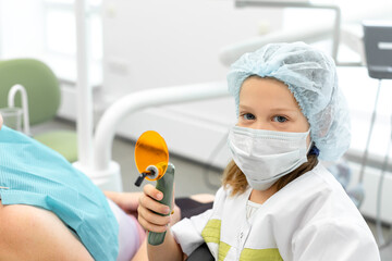 Dental curing light in the hands of a little caucasian girl. A child plays dentist in the dentist's office