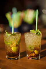 Two glasses of mojito cocktail with fresh lime and mint on a wooden table in a bar or nightclub
