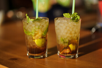 Two glasses of mojito cocktail with fresh lime and mint on a wooden table in a bar or nightclub