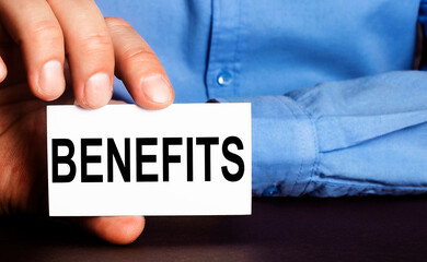 BENEFITS is written on a white business card in a man's hand. Advertising concept