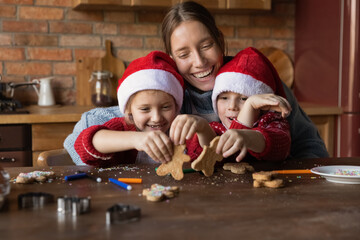 Loving smiling young mom have fun baking Christmas cookies with two little children enjoy winter holidays at home. Happy mother cooking biscuits with small kids get ready for New Year celebration.