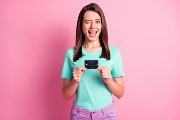 Photo portrait of woman holding credit card in two hands winking isolated on pastel pink colored...