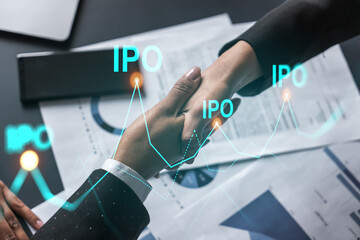 Multiexposure of two businesspeople handshake and initial primary offering, IPO hologram drawing background. Concept of partnership and business boost. Formal wear.