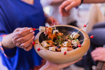 Person taking a skewer from the skewer plate of fresh cheese, salmon and spices tapas in a wooden bowl. Ideal tapas for corporate events, weddings, baptisms, communions.