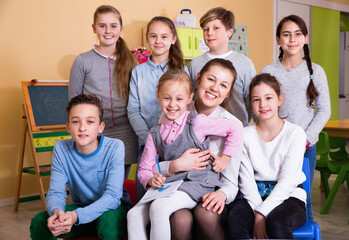 Portrait of friendly smiling positive group of pupils with female teacher sitting in schoolroom
