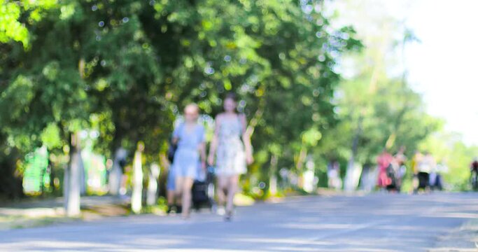 Blurred background of a central park with people walking sunny summer day