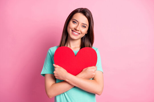 Photo portrait of cute girl hugging embracing red heart shaped paper invitation card isolated on pastel pink color background