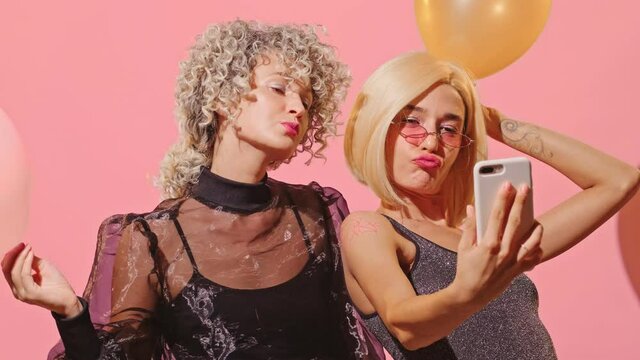 Close up of couple young beautiful fashionable women have fun together, hold balloons to decorate room, pose at camera and make selfie, being in great festive mood, feel energetic. Happy party time.