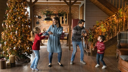 Wide banner panoramic view of happy young Caucasian family with two small kids have fun celebrating Christmas at home. Overjoyed parents with children enjoy New Year winter holidays together.