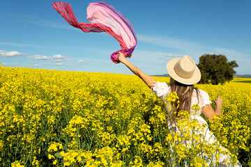 Woman in whte dress and floating scarf in canola field - 388231310