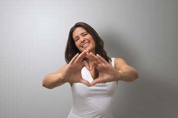 Attractive middle-aged, brunette Spanish woman making heart gesture with hands