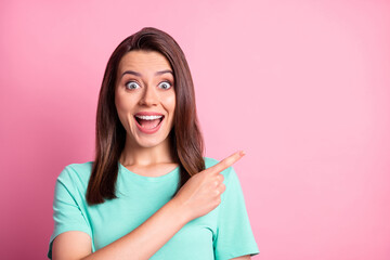 Photo portrait of amazed girl staring pointing on empty space with finger wearing teal t-shirt isolated on pastel pink color background