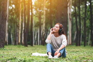 Naklejka na ściany i meble A beautiful young asian woman enjoy listening to music with headphone with feeling happy and relaxed in the park