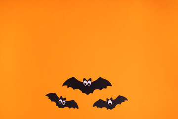Fototapeta na wymiar Cardboard with three bats looking up on orange background. Halloween party wallpaper idea for kids. Great for writing text