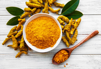 Bowl with turmeric powder and dry roots on a wooden background