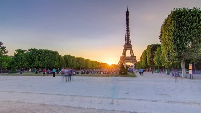 Eiffel Tower seen from Champ de Mars during sunset timelapse, Paris, France. People sitting on lawn and walking around. Summer evening with clear sky