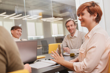 Female entrepreneur laughing, talking to her creative team during meeting at the office