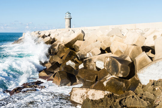 Wave crashing against concrete tetrapods wave breakers with a small lighthouse in the background in the Lebanese coastal town Batroun, Lebanon