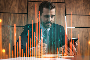 Obraz premium A businessman in office taking notes using phone and stock graph hologram. Multiexposure. Formal wear.