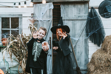 children a boy in a skeleton costume and a girl in a witch costume having fun at a Halloween party on the decorated porch
