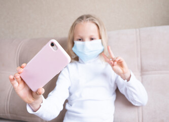 A schoolgirl in a mask looks at the phone at home. The COVID-19 pandemic is forcing children to learn online.