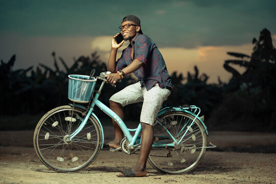 image of african young guy, with mobile phone siting on a  bicycle 