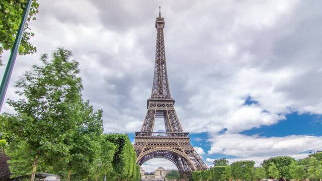 Champ de Mars and the Eiffel Tower timelapse hyperlapse in a sunny summer day. Paris, France. Green trees and cloudy sky, people walking around