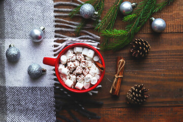Hot cocoa in a red mug with marshmallows and cinnamon on a wooden background with plaid, Christmas balls, pine cones and fir branches. Cozy winter concept.Close-up, selective focus, flat lay, top view