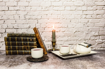 still life of antique books with candles and tea set, a clock is incorporated