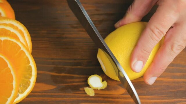 Male hand with big knife slicing lemon citrus fruit on the cutting board at kitchen. cooking process in home, top view