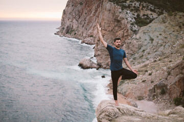 Young man doing yoga exercises on mountain with beautiful sea view.