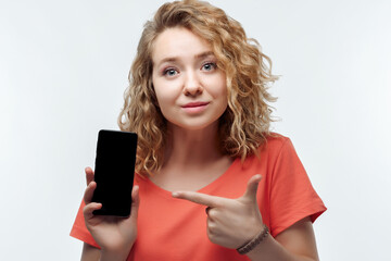 Naklejka premium Young woman Showing Smartphone Blank Screen, looking at Camera Recommending Mobile App