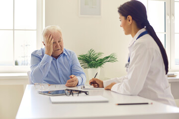 Fototapeta premium Senior man patient complaining on headache to young positive woman doctor