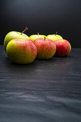 Three ripe fresh green apples and tree red apples on black table and dark background. Free copy space. School snacks or organic food concept