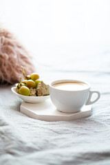 Cup of coffee and grapes with cozy pillow on blanket in home bedroom interior